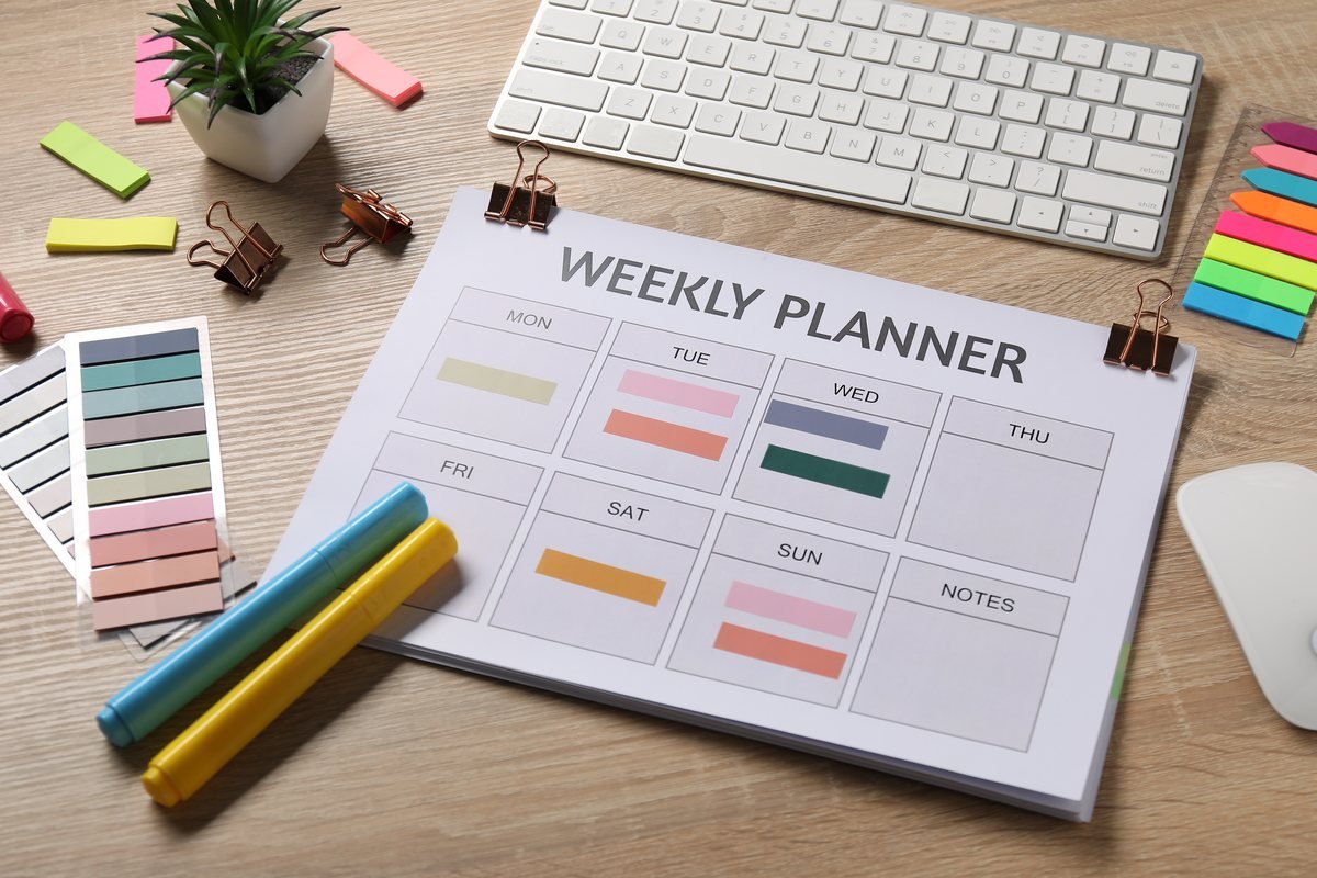 Planner săptămânal pe un birou, cu tastatură, notițe adezive și instrumente de scris | GetVizual