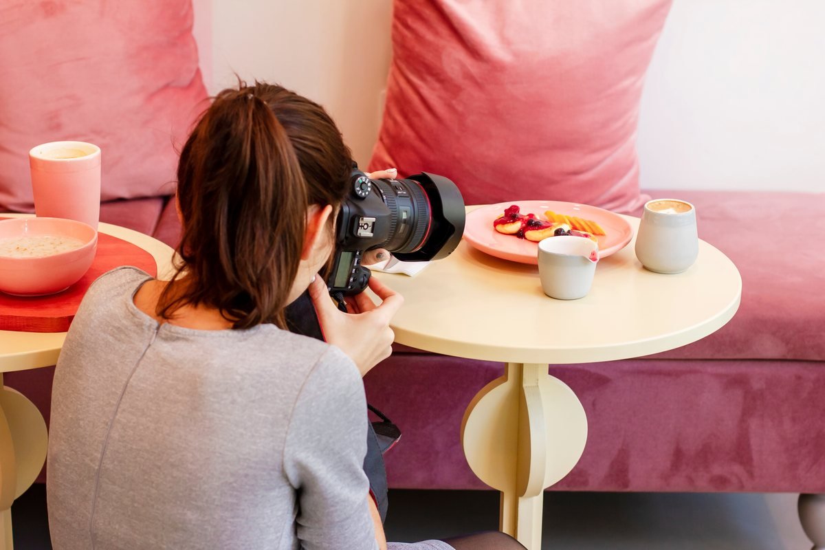 Fotografă care fotografiază mâncarea de pe o masă, într-o cafenea | GetVizual