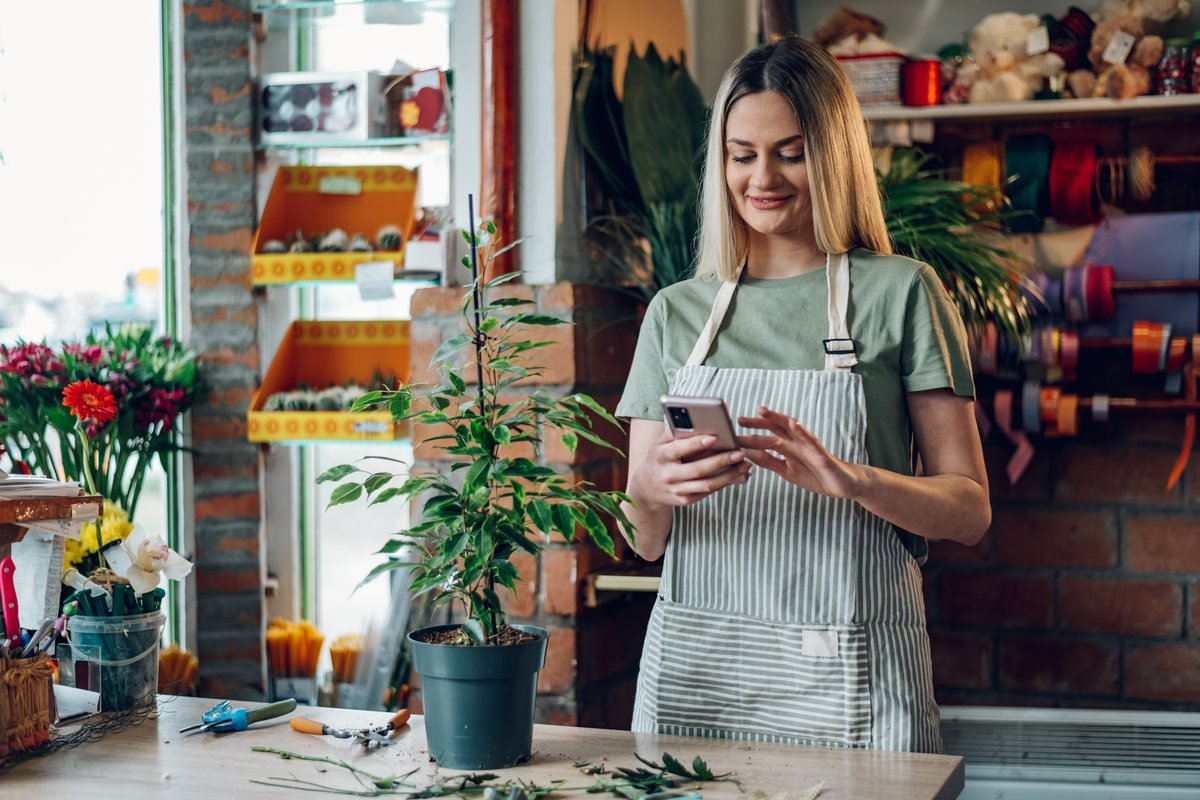 Femeie într-o florărie care folosește telefonul în timp ce lucrează | GetVizual