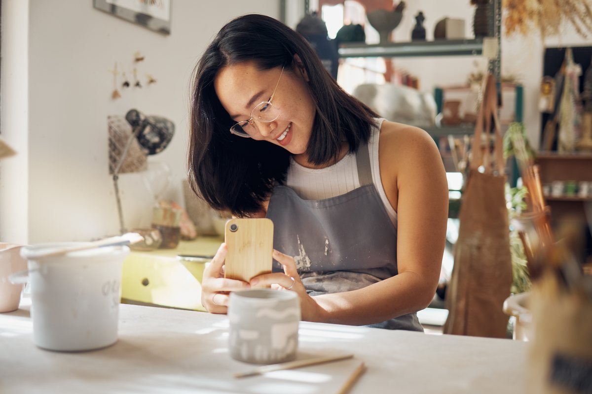 Femeie care fotografiază cu telefonul o ceramică într-un atelier | GetVizual