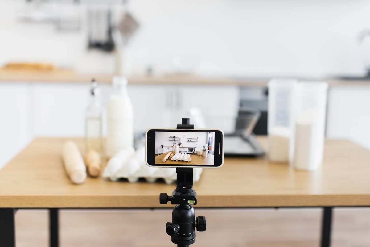 Telefon montat pe trepied pe o masă din bucătărie, cu ingrediente în fundal | GetVizual