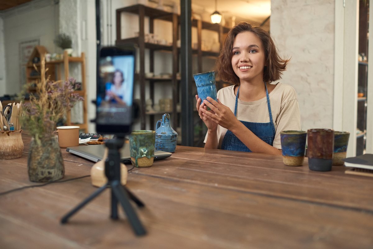 Femeie într-un atelier de ceramică care prezintă o piesă în fața unui telefon montat pe trepied | GetVizual
